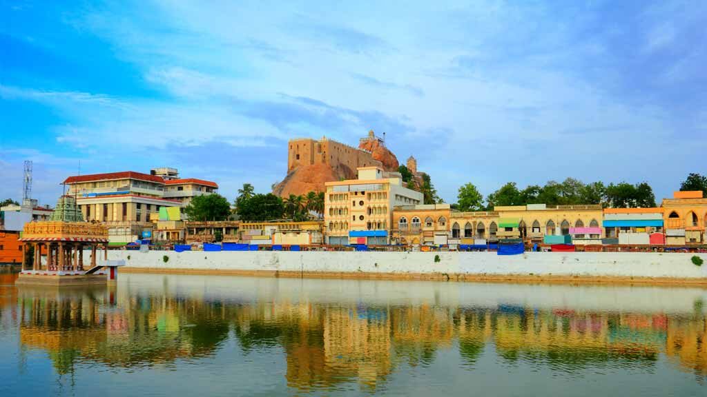 Beautiful scenic view of Trichy (Tiruchirapalli) city with colorful houses, ancient Rock Fort (Rockfort) and Hindu temple reflected at calm pond water, Tamil Nadu, India, South Asia